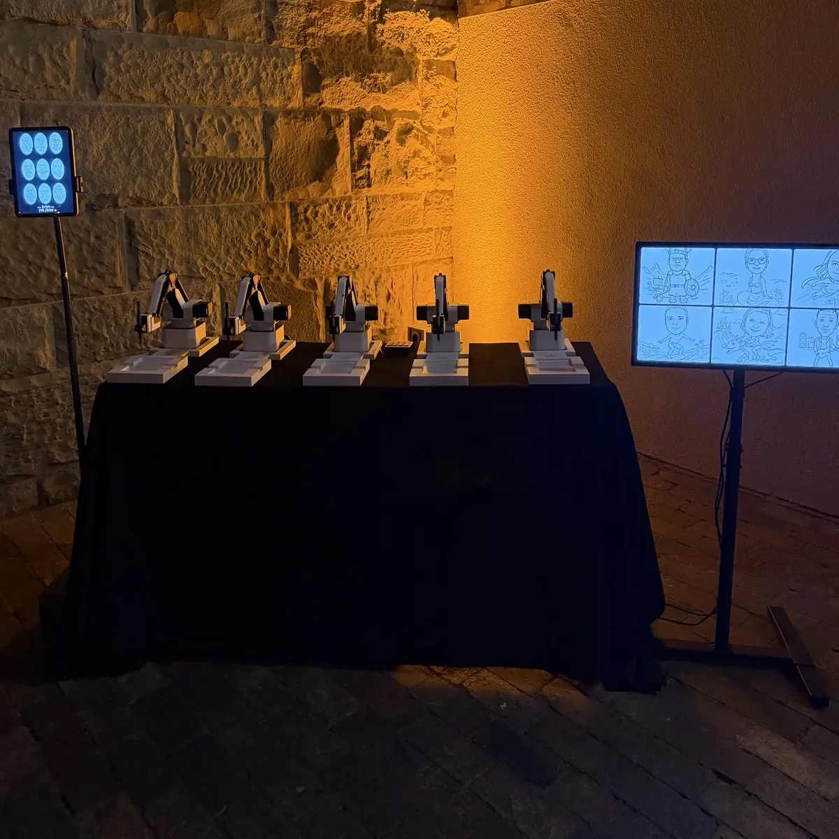 Fünf KI Zeichenroboter vor der beleuchteten Natursteinwand der Phönixhalle im Römerkastell Stuttgart, daneben ein Monitor mit gezeichneten Porträts