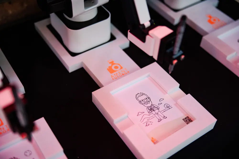 Close-up: Roboterarm zeichnet Portrait auf Papier mit Ament-Fotobox-Logo